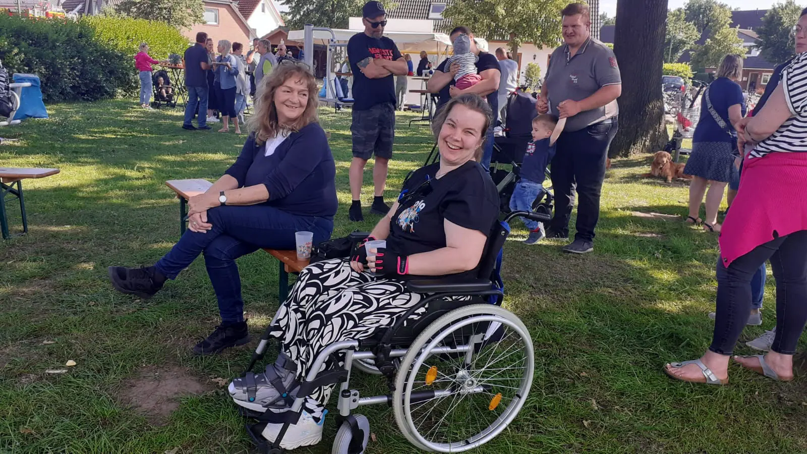 Zwei lächelnde Frauen, eine im Rollstuhl, auf der Festwiese